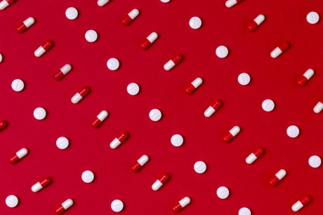 Ein Bild, dass weiße runde Pillen und rot-weiße Kapseln diagonal im Wechseel aufgereiht auf roten Fonds zeigt