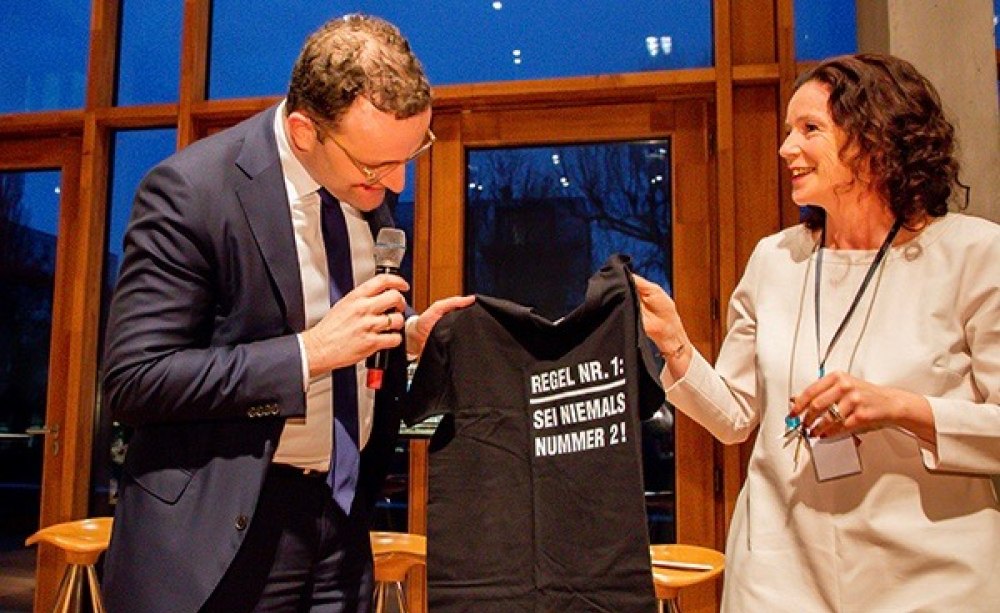 Eine der Initiatorinnen, Cornelia Wanke, überreicht Bundesminister Spahn ein T-Shirt mit der Aufschrift: „Regel Nr. 1: Sei niemals Nummer 2!“.