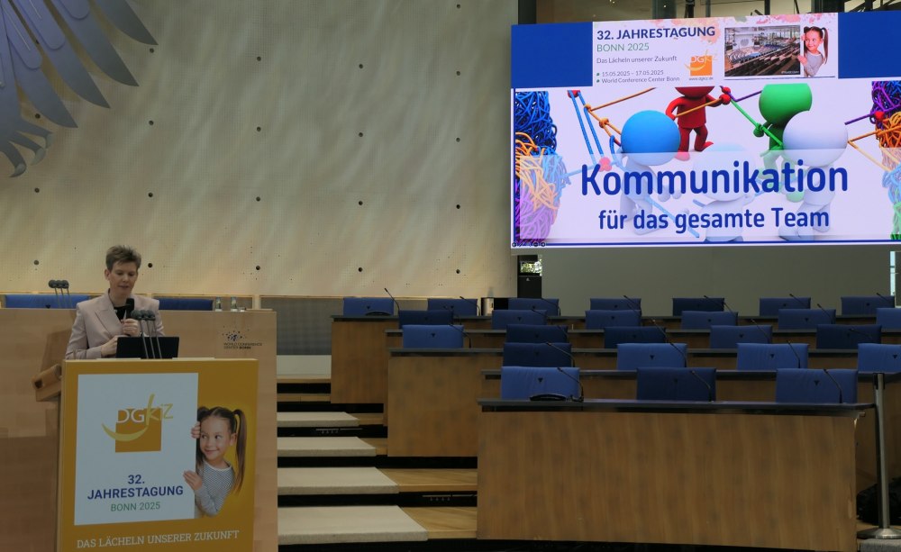 Frau spricht an Pult, im Hintergrund große Präsentationsleinwand