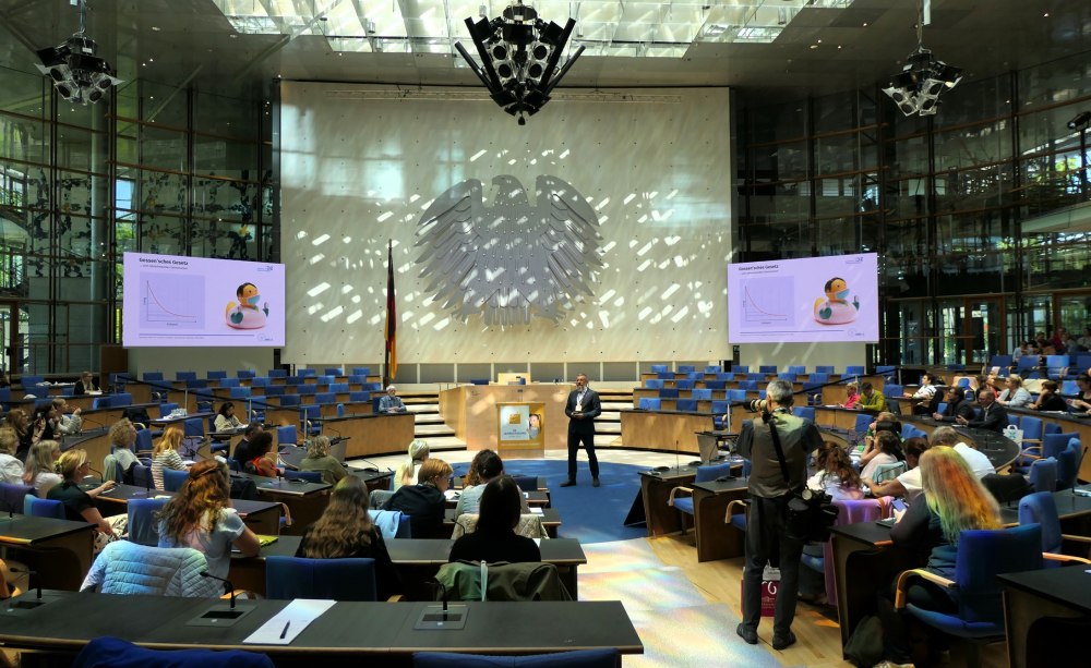 großer Plenarsaal mit Bundesadler an der Wand, ein Mann steht in der Mitte und spricht