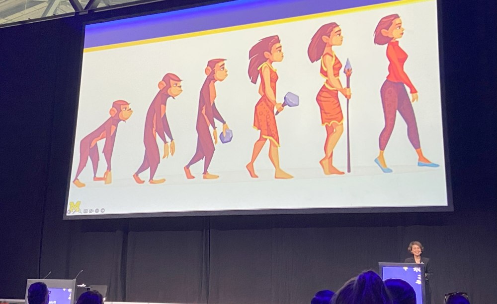 Eine Frau an einem Podium, hinter ihr eine Präsentation auf einer Videoleinwand