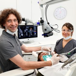 Dr. Lang mit Mikroskop und Helferin bei der Patientenbehandlung
