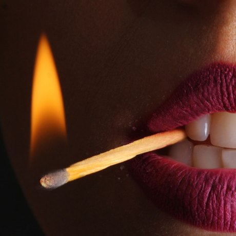 Nahaufnahme von einer Frau mit einem brennenden Streichholz im Mundwinkel