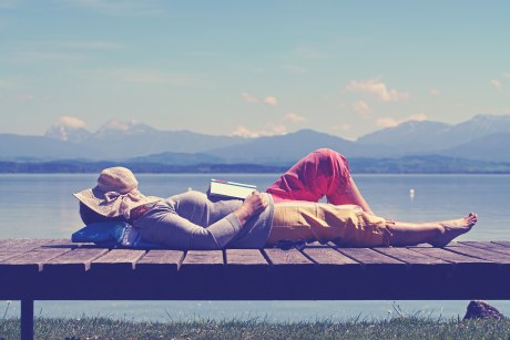 Frau schläft  auf einem Steg vor einem Bergsee