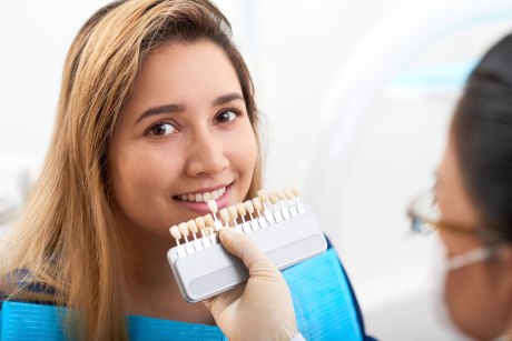 Frau beim Zahnarzt wird verschieden farbige Zahnkronen gezeigt
