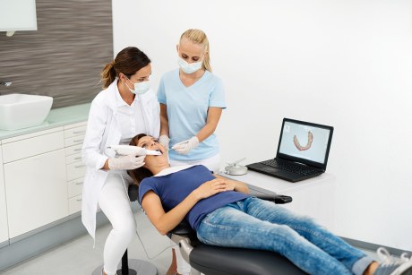 Frau auf Zahnarztstuhl wird mit Intraoralscanner untersucht