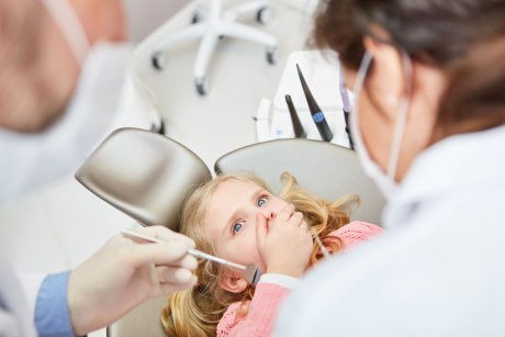 Kleines Mädchen auf dem Zahnarztstuhl hält sich den Mund zu