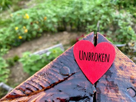 Auf altem Holz liegt ein rotes Herz mit dem Schriftzug "UNBROKEN"