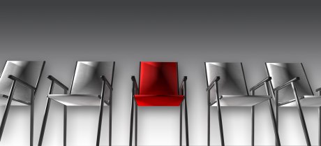 Ein Bild, das fünf Stühle in leichter Untersicht zeigt, Das bild ist in schwarz-weiß, nur der mittlere Stuhl ist knallig rot.