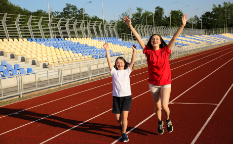 Zwei Mädchen, eines mit Down-Syndrom laufen jubelnd über Sportplatz