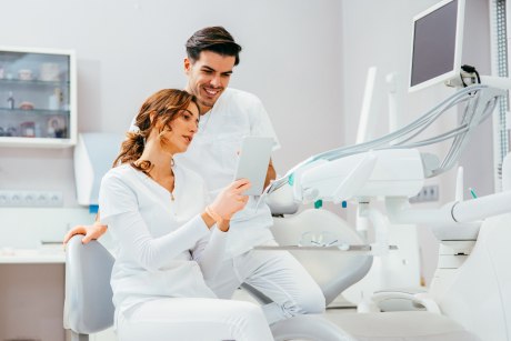 eine Frau und ein Mann schauen auf ein Tablet, im Hintergrund Zahnarztgeräte
