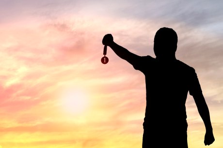 Silhouette eines Mannes mit gestrecktem Arm und Medaille in der Hand vor Sonnenuntergang