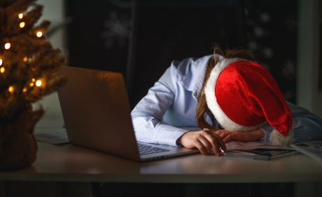 Frau mit Nikolausmütze legt erschöpft den Kopf neben einen laptop im Halbdunklen
