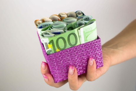 Eine Frauenhand hält eine violette Geschenkschachtel in der Hand, die mehnrere Euroscheine enthält