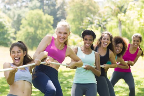 Sechs junge Frauen in Sportkleidung ziehen lächelnd gemeinsam an einem Tauende