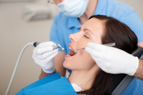 Frau mit offenem Mund, Zahnarzt hält Instrumente in behandschuhten Händen