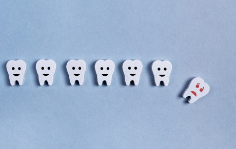 Ein Bild, das auf hellblauen Fonds sechs Smiley-Zähne in einer Reihe zeigt und einen unglücklichen Smiley-Zahn der aus der Reihe nach unten fällt.