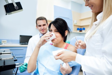 Frau in Zahnarzt-Behandlungsstuhl mit Wasserbecher am Mund