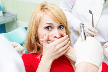 Frau auf dem Behandlungsstuhl des Zahnarztes hält sich ängstlich den Mund zu