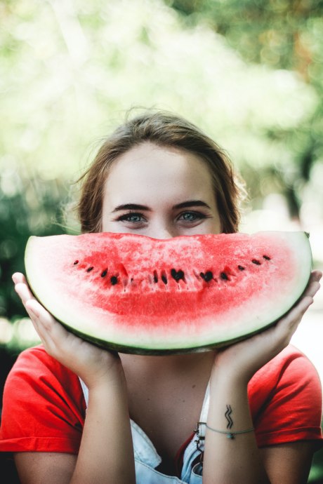 Frau hält sich eine halbe Scheibe Wassermelone vor das Gesicht
