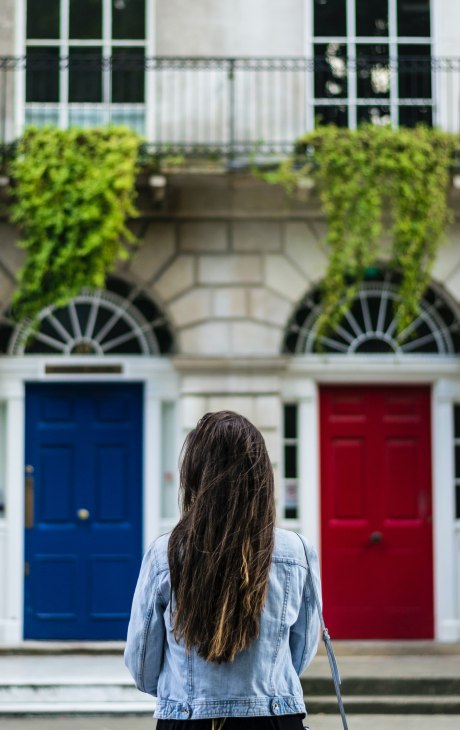 Junge Frau von Hinten betrachtet steht vor zwei Türen - eine blau, die andere rot