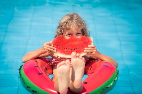 Kind mit großem Stück Melone im Pool in einem Schwimmring