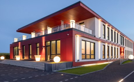 Modernes zweigeschosiges Gebäude mit rot-weißer Verkleidung im Abendlicht