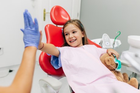 Kind im Zahnarztstuhl klatscht lachend behandschuhte Hand ab