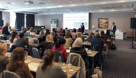 Beamer-Präsentation mit an Tischen sitzendem Publikum