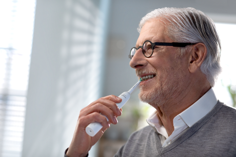 Älterer Mann putzt sich mit elektrischer Zahnbürste die Zähne
