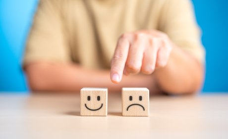 Hand making a decision between two wooden cubes with happy and sad face for positive or negative mindset selection. Emotional state and mental health concept. Like or Dislike for client satisfaction. 