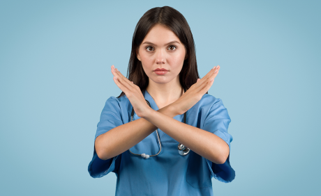 Medizinische Fachangestellte mit blauem Kittel formt mit ihren Armen vor dem Körper ein X.