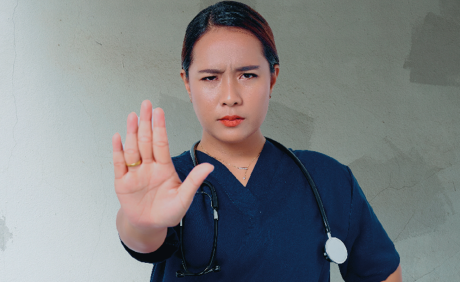 Plakatmotiv der Kampagne „Praxis in Not“, medizinische Fachangestellte in blauer Dienstkleidung streckt die Flache Hand nach vorne aus und signalisiert "Stop".