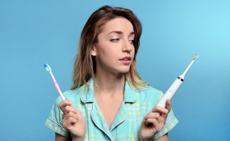Frau hält normale und elektrische Zahnbürste