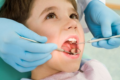 Kleiner Junge auf dem Behandlungsstuhl mit geöffnetem Mund und zahnmedizinischen Behandlungsinstrumenten