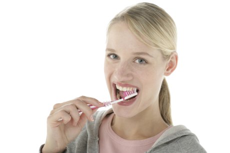 Eine Frau hält eine pinke Handzahnbürste an ihre Zähne