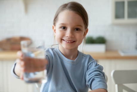 Ein junges Mädchen lächelt und hält ein Glas Wasser in die Kamera