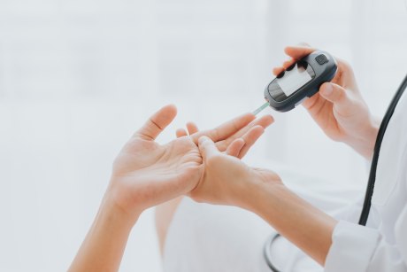 Arzt benutzt Glukosemesser zur Überprüfung des Blutzuckerspiegels aus der Hand des Patienten