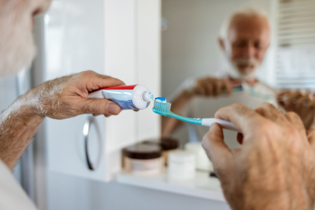 Alter Mann putzt sich vorm Spiegel die Zähne