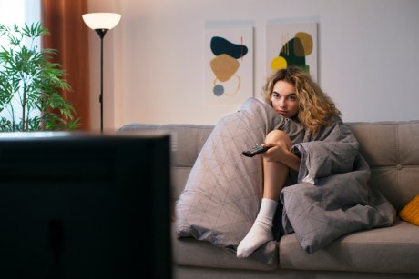Frau in eine Decke gehüllt sitzt vor dem Fernseher 