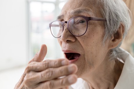 Alte Frau hält eine Hand vor den geöffneten Mund