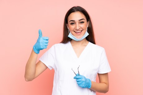 Zahnmedizinische Mitarbeiterin zeigt Daumen hoch mit Handschuhen 