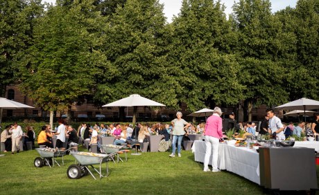 Wiese, viele Tische und Bänke mit Menschen, Buffet, Schubkarren mit Getränken