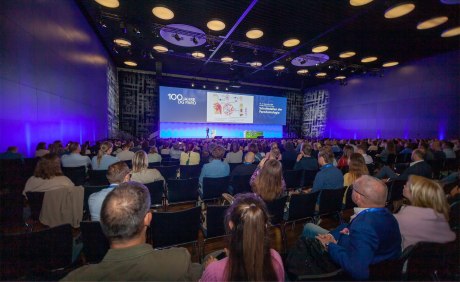 Zuschauer im Auditorium blickend auf Schriftzug 100 Jahre DG Paro auf der Leinwand