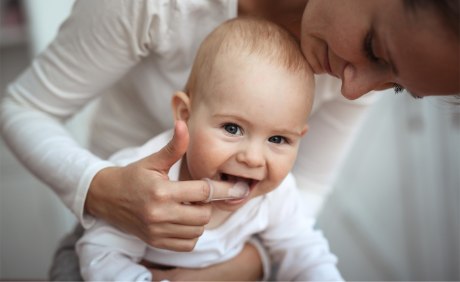 Mutter beugt sich zur Zahnpflege über zahnendes Kleinkind