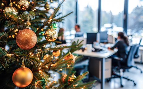 vorne ein geschmückter Weihnachtsbaum, im Hintergrund Menschen an Schreibtischen 