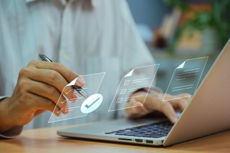 Person am Notebook, eine Hand an der Tastatur, die andere klickt mit Stift auf virtuelle Dokumente