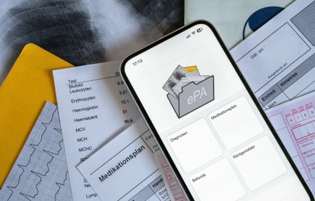 Smartphone mit ePA-App dahinter medizinische Unterlagen in Papier
