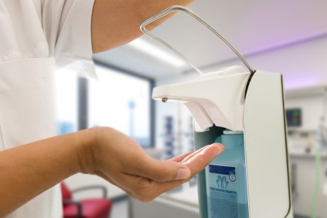 medizinisches Personal hält Hand unter Desinfektionsspender, der mit dem Ellbogen heruntergedrückt wird