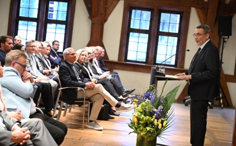 sitzendes Publikum, festlich geschmückter Raum, ein Mann spricht am Podium